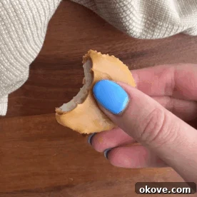 A close-up of a hand holding a single peanut butter banana bite, showing the distinct layers of banana and peanut butter