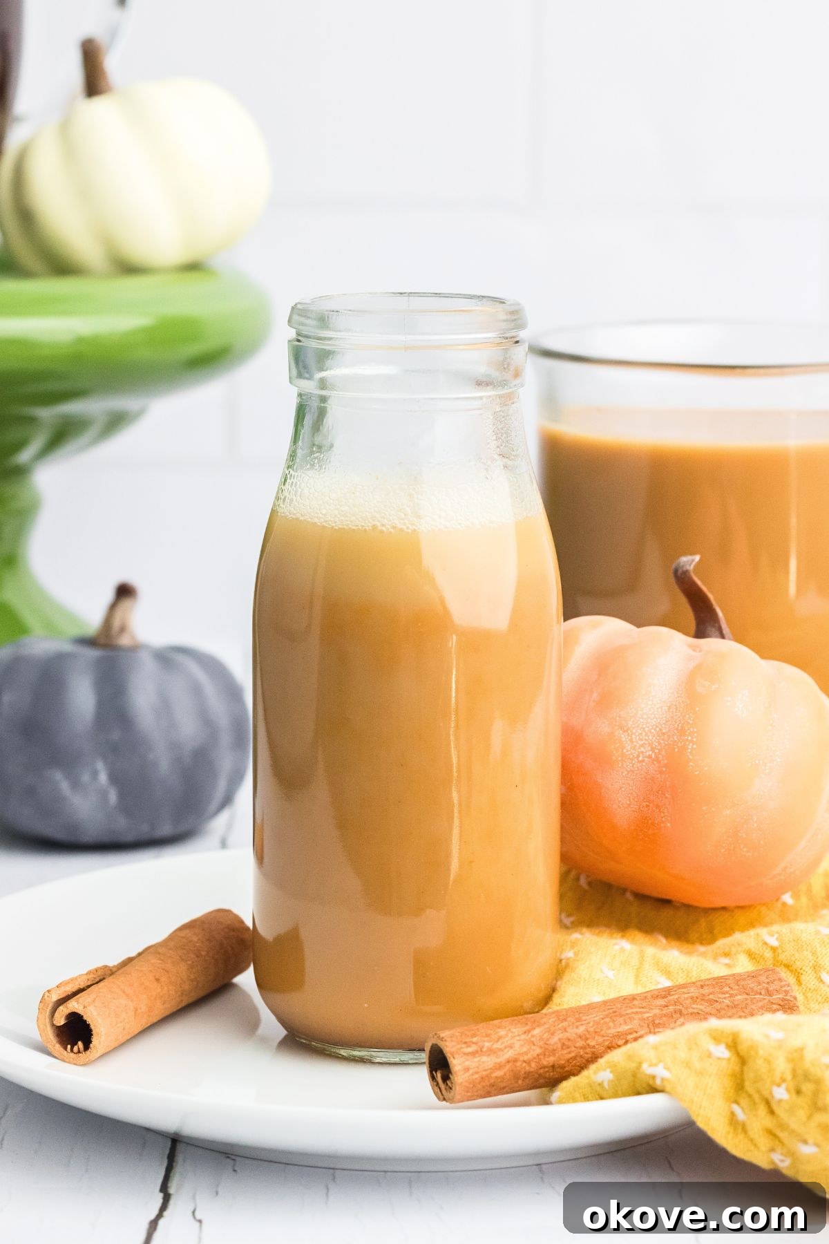 Pumpkin spice creamer in a small bottle on a white plate with cinnamon sticks and small pumpkins on the table, evoking cozy fall vibes.