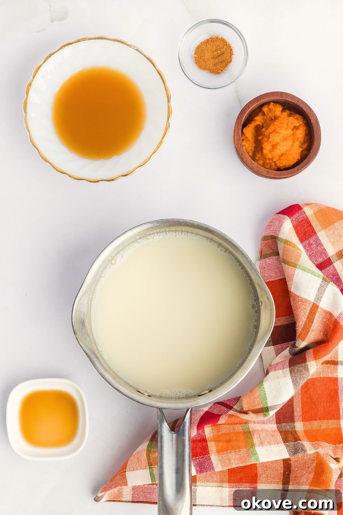Ingredients needed to make pumpkin spice creamer measured into small bowls on a white marble table, ready for mixing.