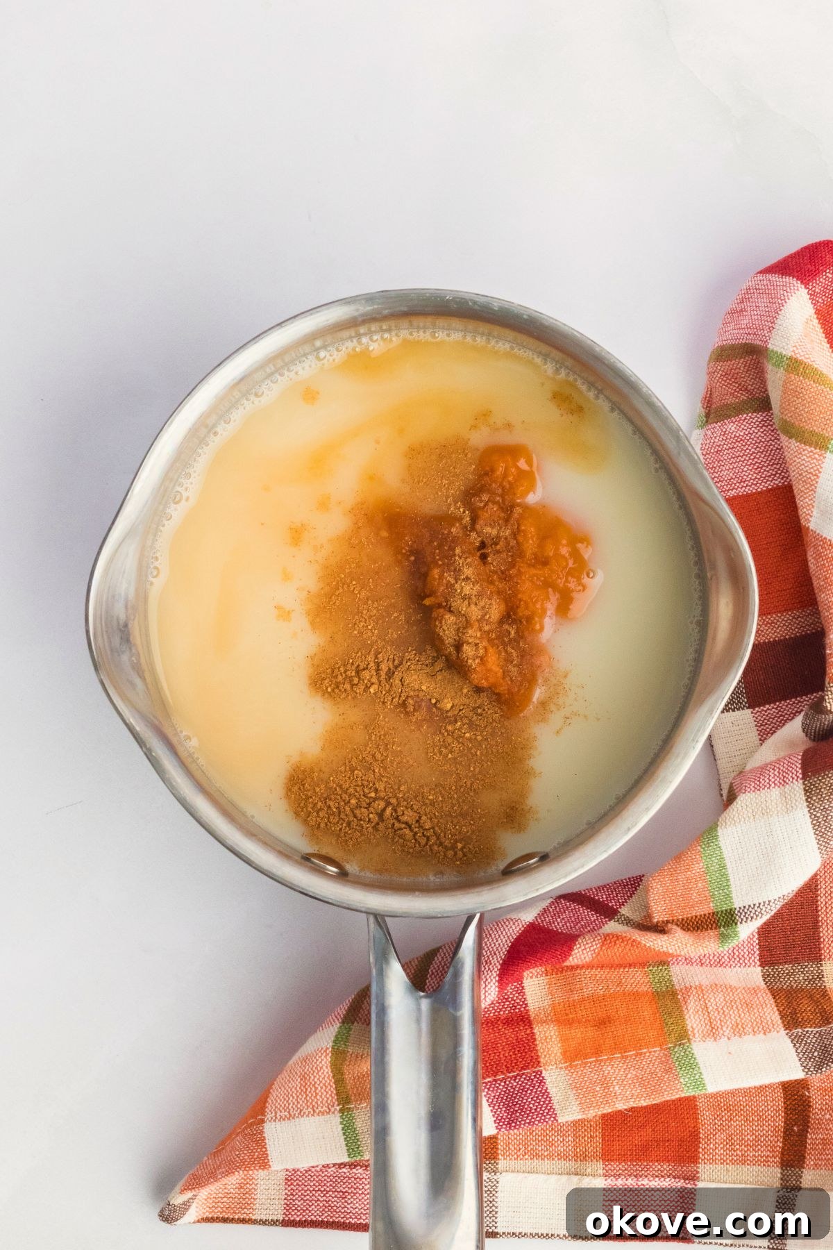 Pumpkin puree and other ingredients in a small saucepan on a white table, being whisked together.