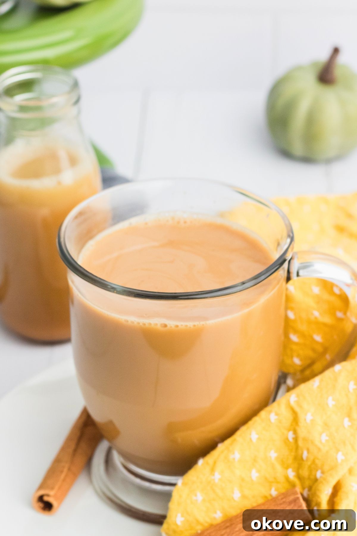 Creamy coffee in a clear glass cup with a bottle of pumpkin spice creamer on the table behind it, ready to be enjoyed.