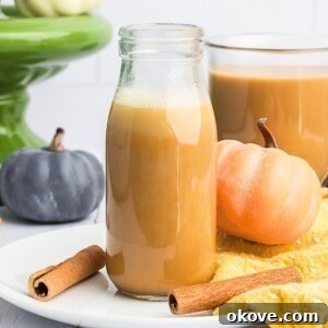Creamy pumpkin spice creamer in a clear glass bottle with small pumpkins around it.