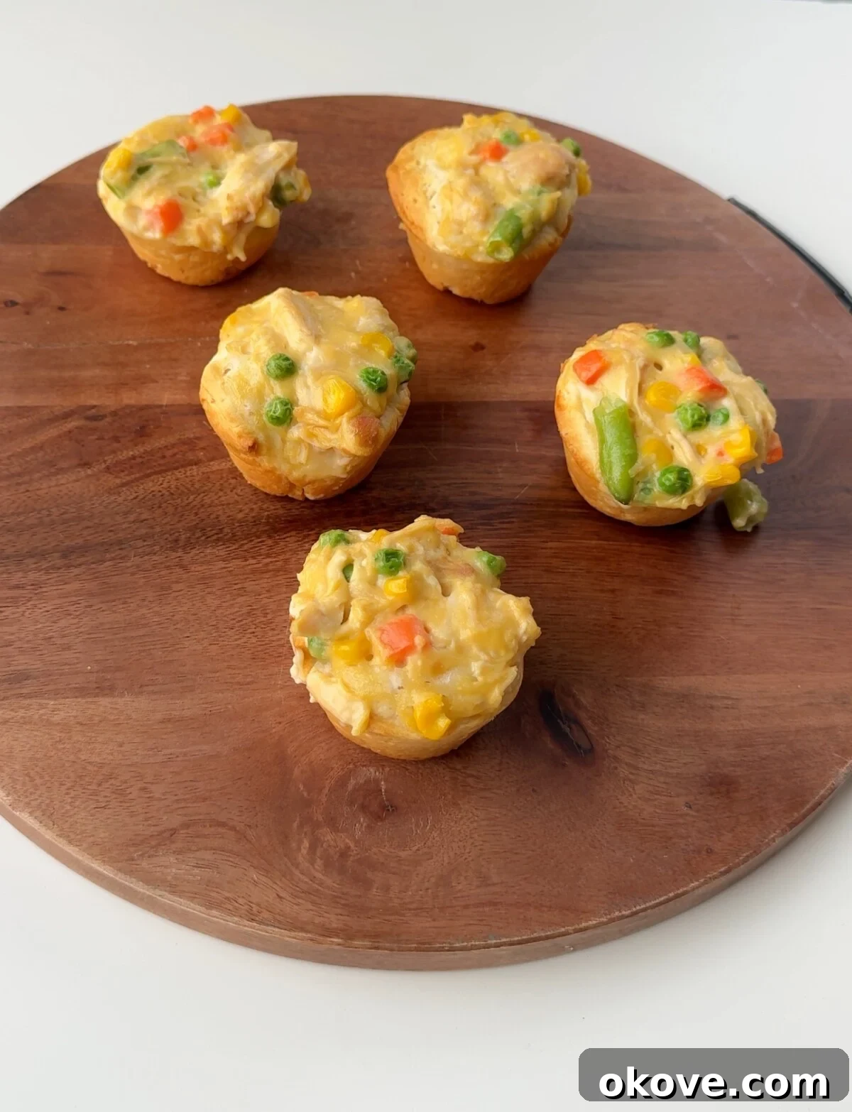 Bite-Sized Chicken Pot Pies 2 A close-up shot of several golden-brown mini chicken pot pies in a muffin tin, garnished with fresh herbs, ready to be served. The flaky crust and creamy filling are visible.