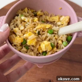 A close-up of a round bowl of Easy Fried Rice, showing the fluffy rice, green peas, and bits of scrambled egg.