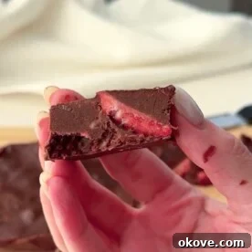 Close-up of frozen berry chocolate fudge squares on parchment paper, showing layers of chocolate and berries.