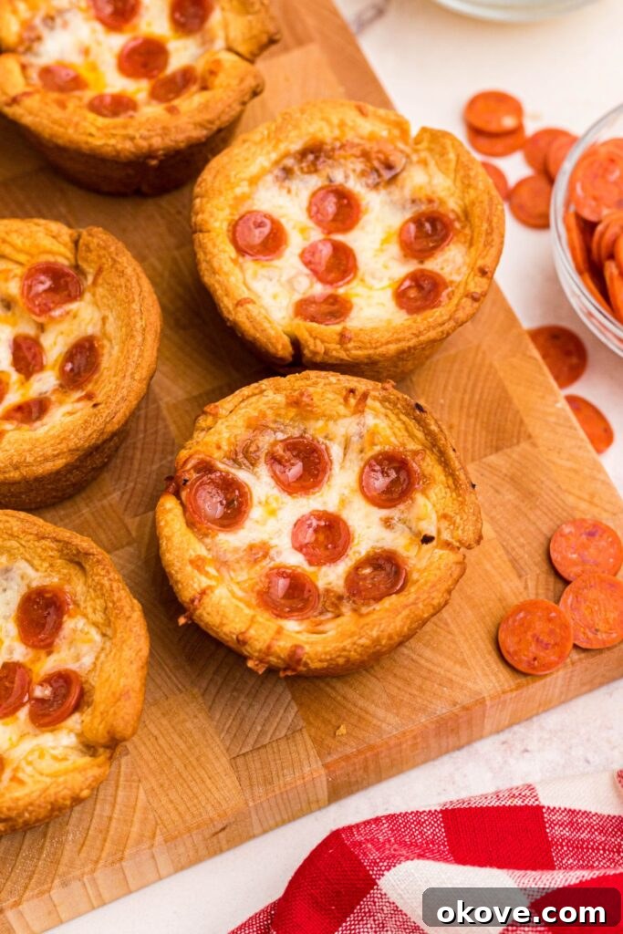 Muffin Tin Pizzas 2 Golden pizza cupcakes on a wooden cutting board with mini pepperonis scattered around it.
