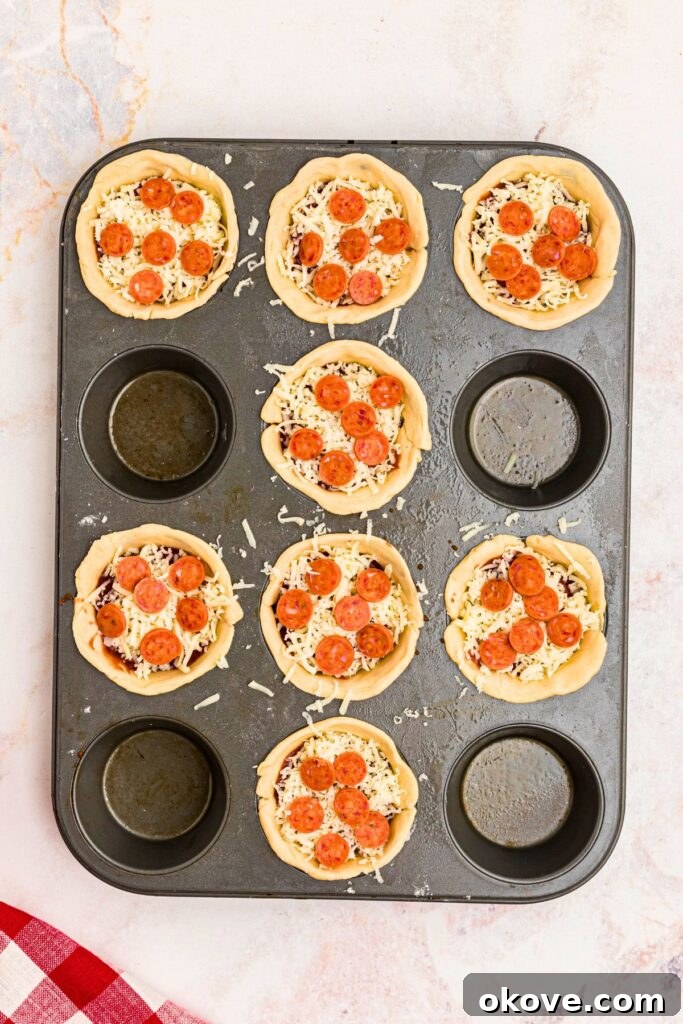 Muffin Tin Pizzas 5 Uncooked pizza cupcakes in a muffin pan, topped with mini pepperonis.