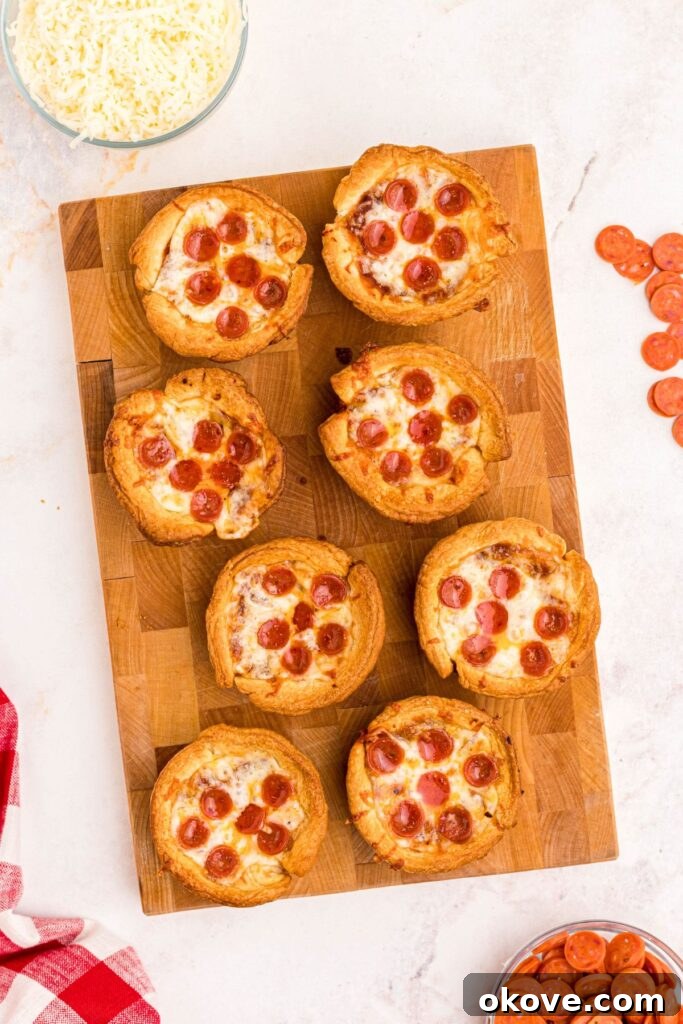 Muffin Tin Pizzas 6 Golden crispy mini pizza cupcakes on a wooden cutting board, with mini pepperonis scattered on a marble table.