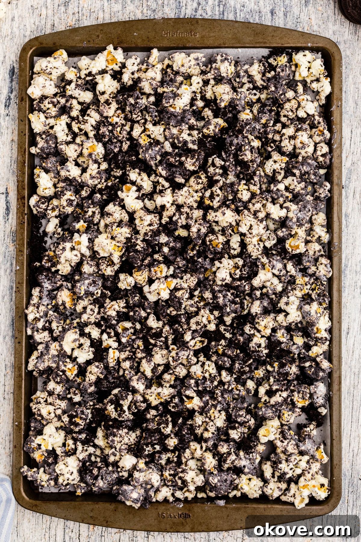 The completed mixture of white chocolate, crushed Oreos, and popcorn, spread out and cooling on a baking sheet lined with parchment paper.
