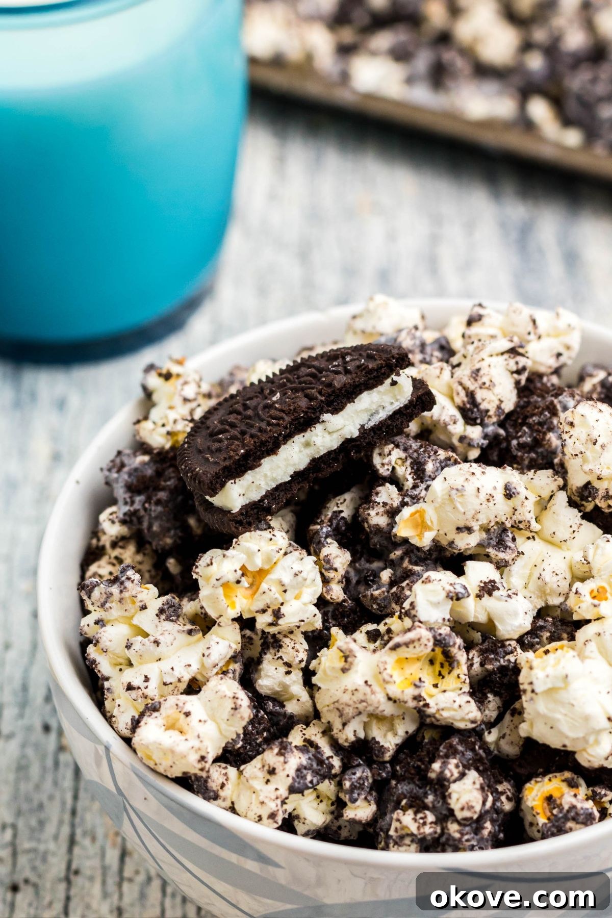 A close-up view of a broken Oreo cookie resting in a bowl of popcorn, highlighting the delicious cookie crumbs mixed throughout.