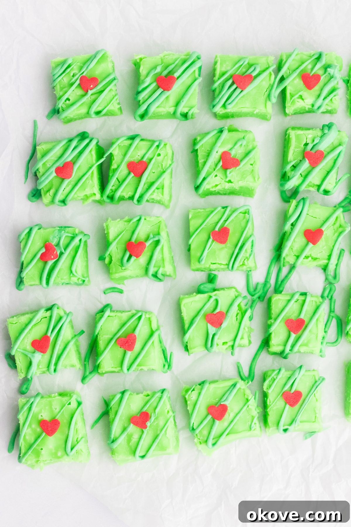 Grinch's Heart-Melting Fudge 7 Bright green Grinch fudge, cut into squares on parchment paper with small red hearts added to the tops of each piece. They are perfectly shaped.