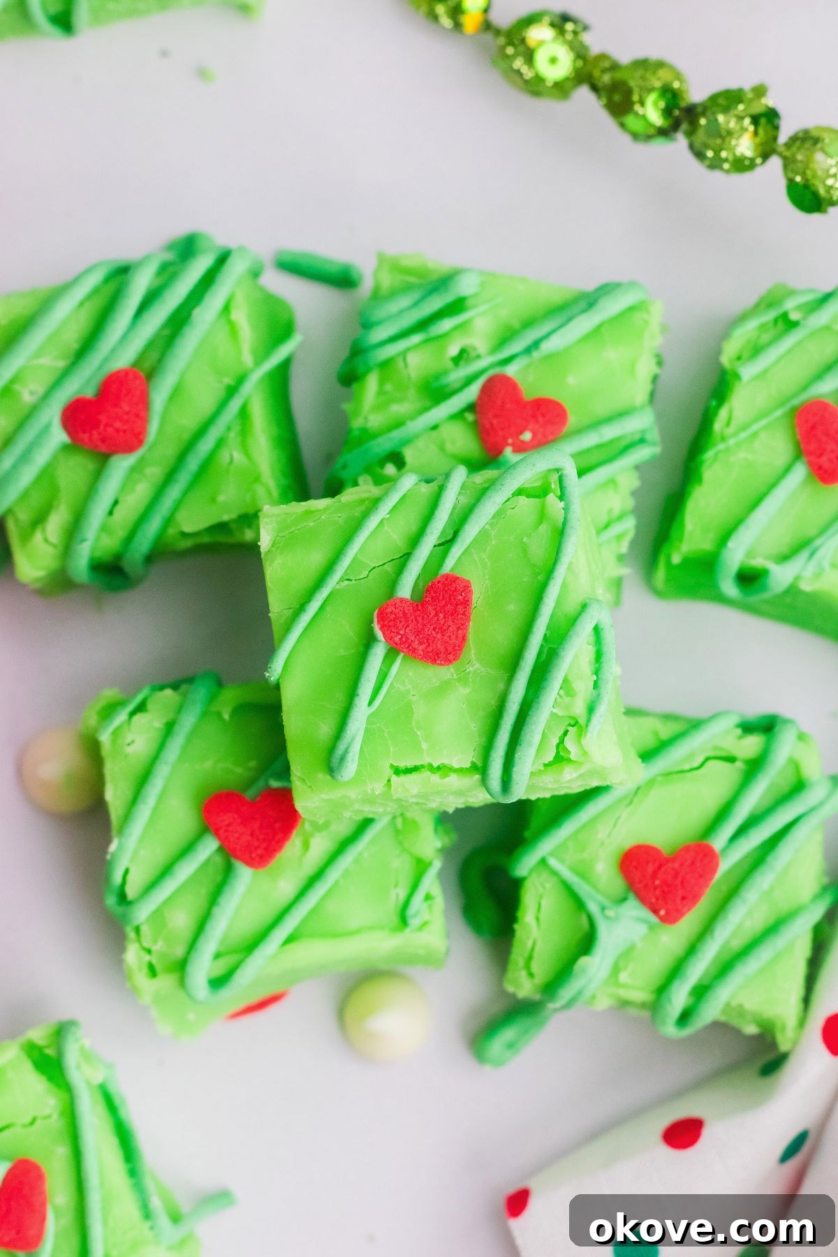 Grinch's Heart-Melting Fudge 8 Square green fudge pieces topped with small red hearts, stacked on a white table. A beautiful holiday display.