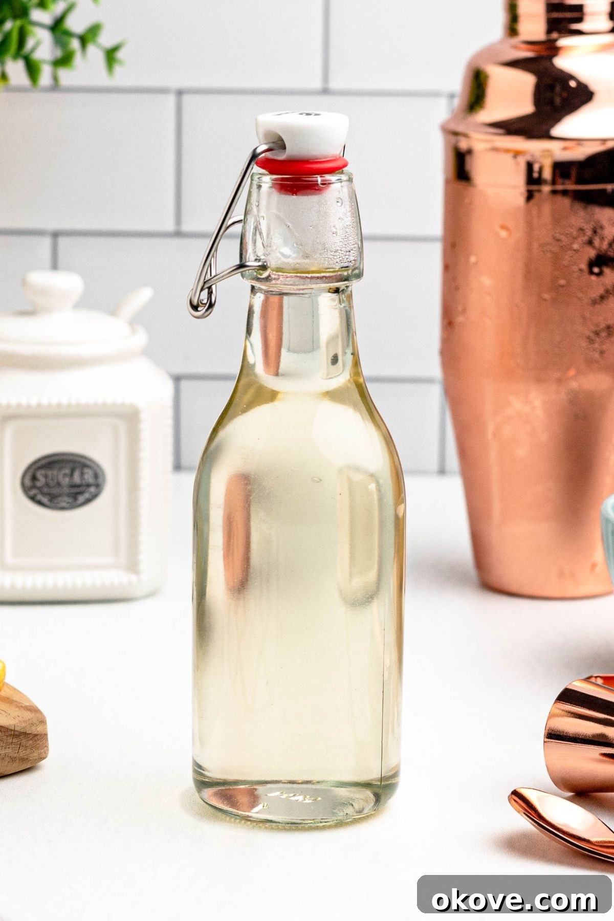 Effortless Simple Syrup for Perfect Drinks 2 Clear glass bottle of simple syrup on a table, with lemon slices and bar mixing tools next to the bottle.