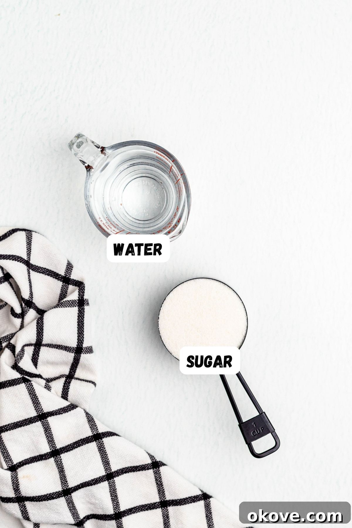 Effortless Simple Syrup for Perfect Drinks 3 Measuring cup of sugar and measuring cup of water, labeled on a table with a black and white linen.