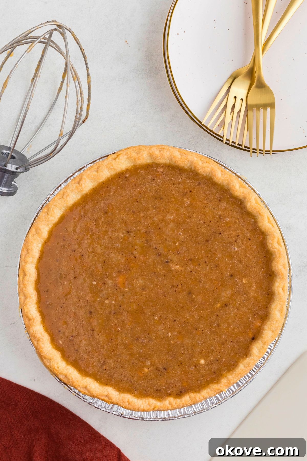 Classic Sweet Potato Pie 6 An uncooked sweet potato pie, with its smooth, vibrant orange filling nestled in a perfectly crimped golden crust, positioned in front of a stack of small white plates.