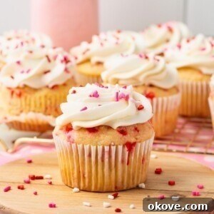 White cupcakes with pink sprinkles baked in the batter, then frosted with white frosting and topped with pink sprinkles.