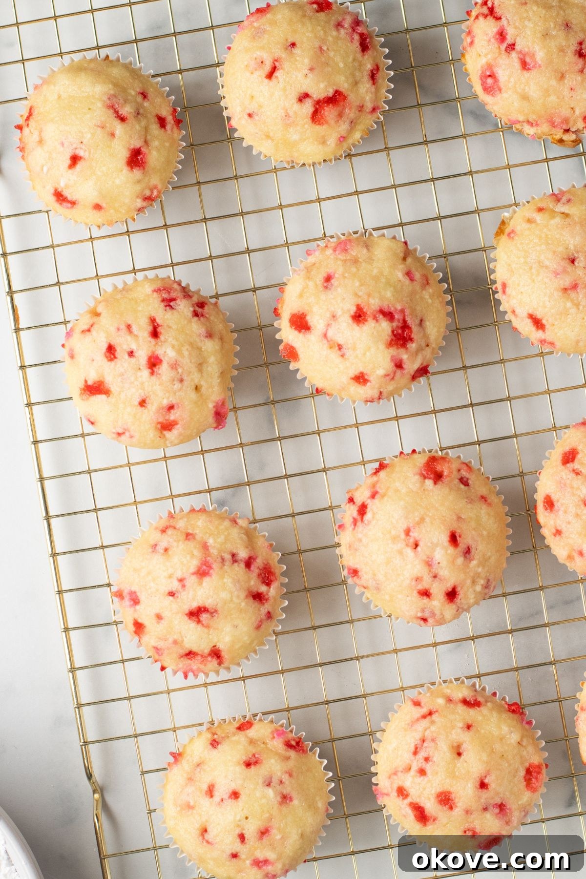 Blushing Sweet Treats 8 Baked cupcakes with pink sprinkles in them, on a cooking rack.