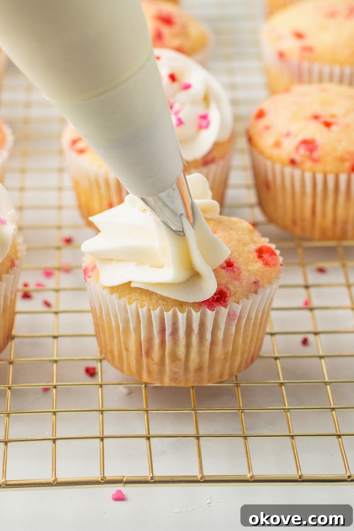 Blushing Sweet Treats 9 Pink sprinkled cupcake being frosted with buttercream frosting.