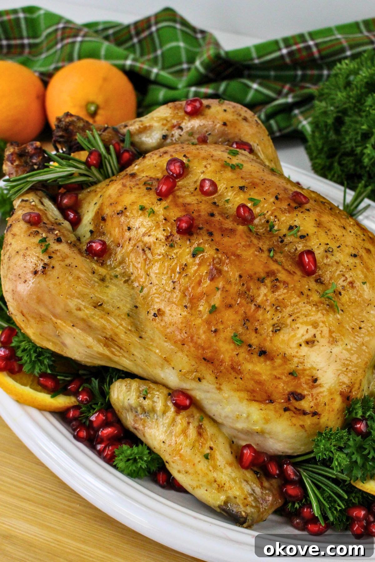 Golden brown roasted chicken on a platter with pomegranate seeds and oranges as garnish, ready for a festive Christmas dinner.
