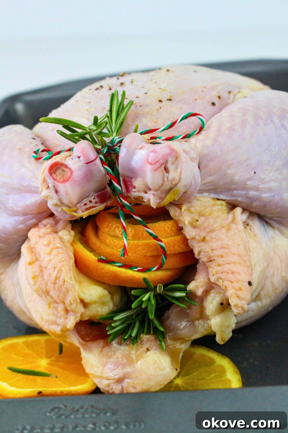 Uncooked chicken, carefully stuffed with orange slices, fresh rosemary, and garlic, now trussed with kitchen twine to maintain its shape during roasting.