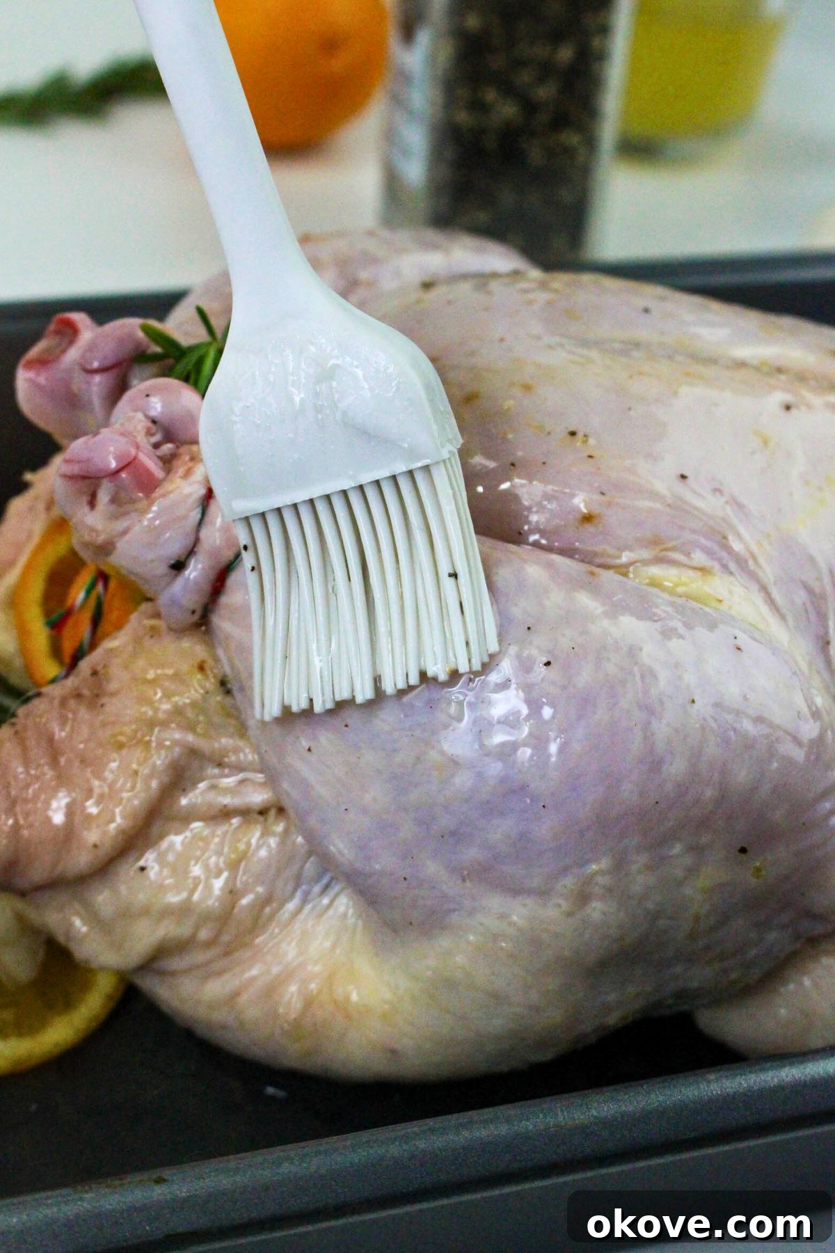 The uncooked chicken being brushed with olive oil and seasoned, prior to being placed in the oven for roasting.