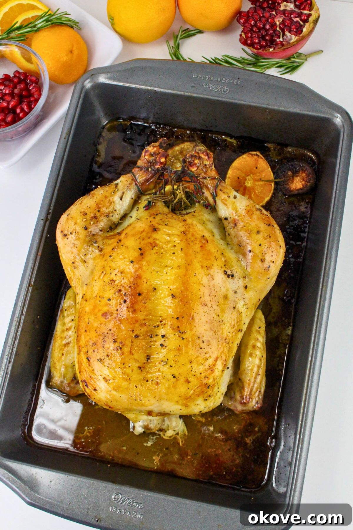 A perfectly golden roasted chicken resting in its roasting pan, surrounded by flavorful pan juices, ready to be served.