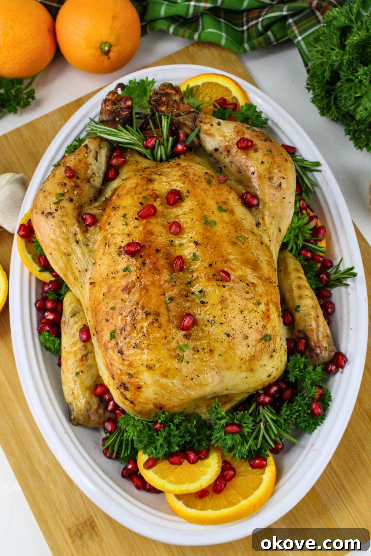Golden roasted chicken, perfectly cooked, presented on a white platter and garnished with fresh parsley and vibrant pomegranate seeds.
