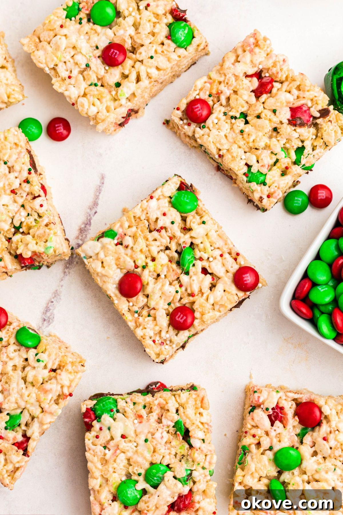 Rice krispie treats with red and green m and m's mixed in, cut into squares, laid out on a marble table.