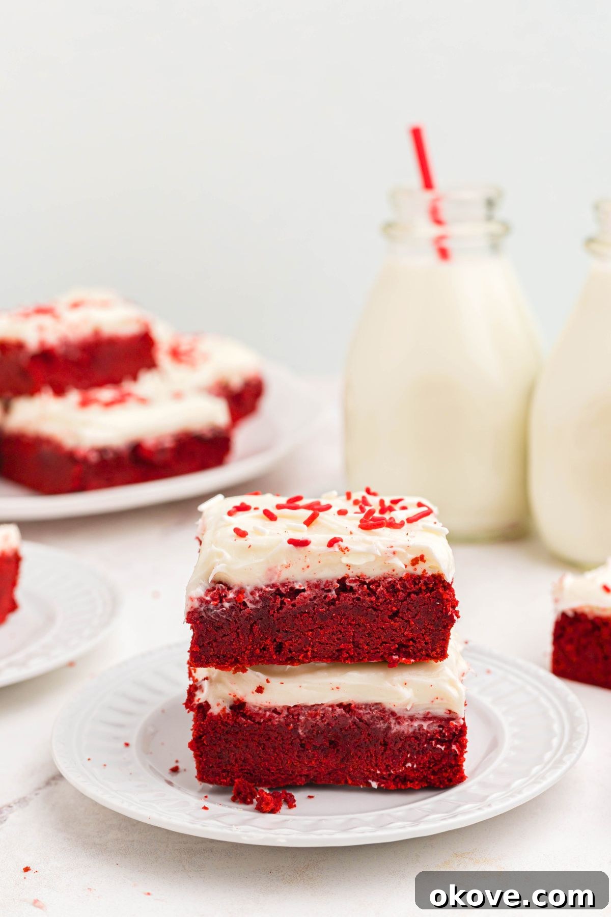Scarlet Velvet Delights 2 Bright red velvet bars stacked elegantly on a white plate, with a glass of milk visible in the soft background.
