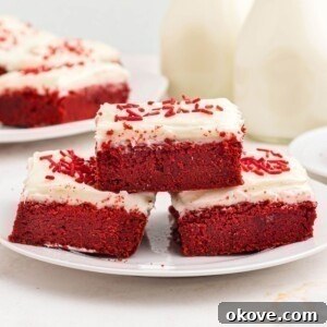 Scarlet Velvet Delights 11 Red velvet bars frosted with cream cheese frosting, stacked on a white plate, ready to serve.