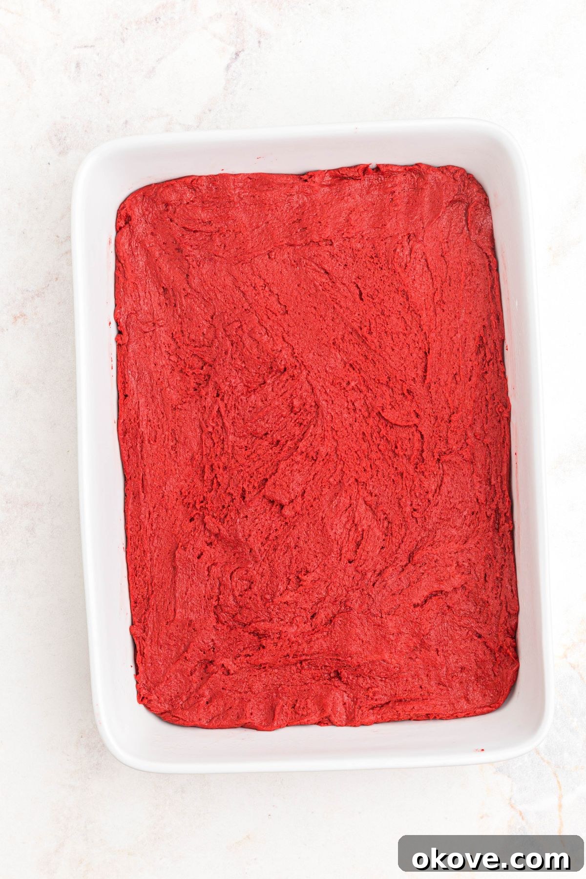Scarlet Velvet Delights 5 Vibrant red velvet batter evenly spread in a white 9x13 inch baking pan, ready for baking.