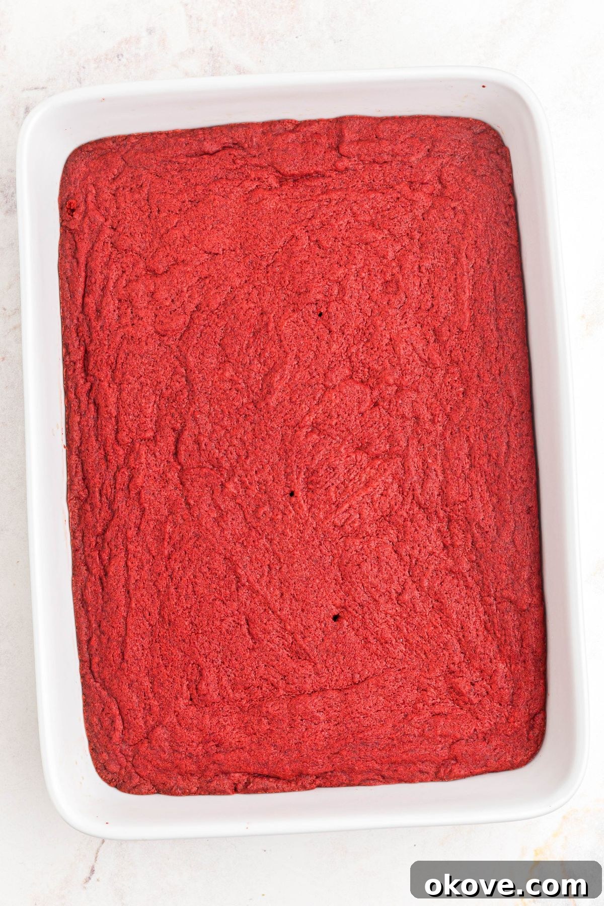 Scarlet Velvet Delights 6 Freshly baked red velvet cookie bars, golden-brown and still warm, resting in a white 9x13 inch baking dish.