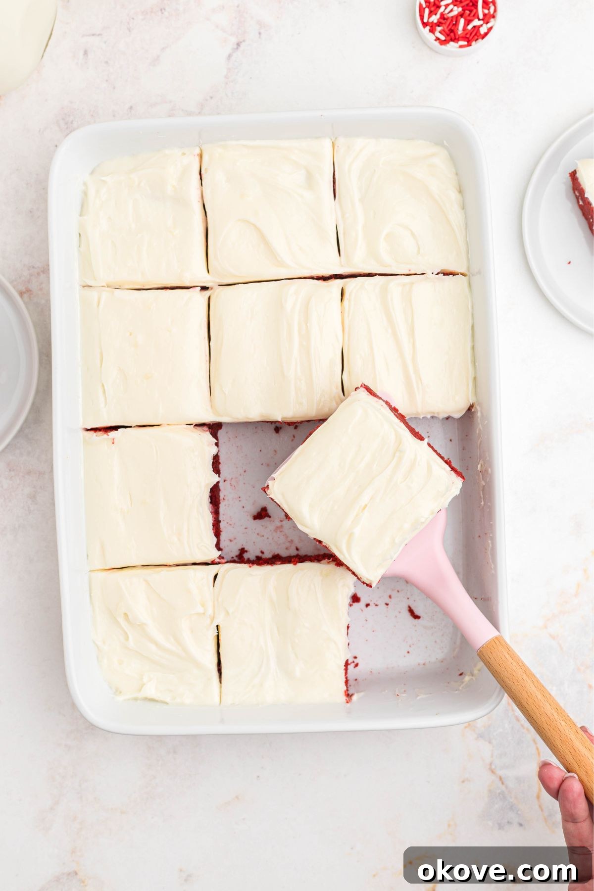 Scarlet Velvet Delights 7 A baking dish filled with vibrant red velvet bars generously topped with smooth, white cream cheese frosting.