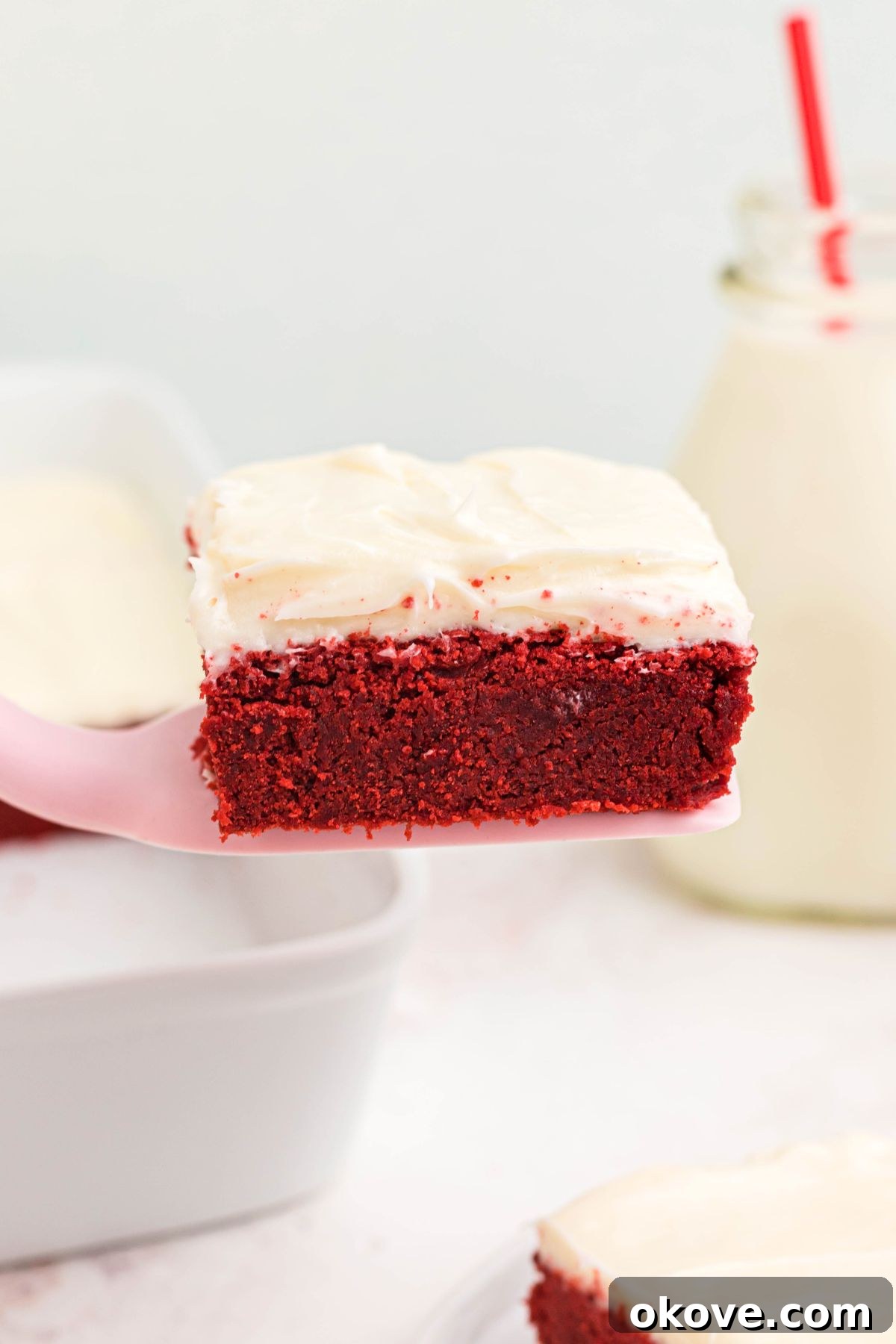 Scarlet Velvet Delights 8 A single red velvet bar, perfectly cut and lifted on a pink spatula, showcasing its fluffy texture and rich frosting.