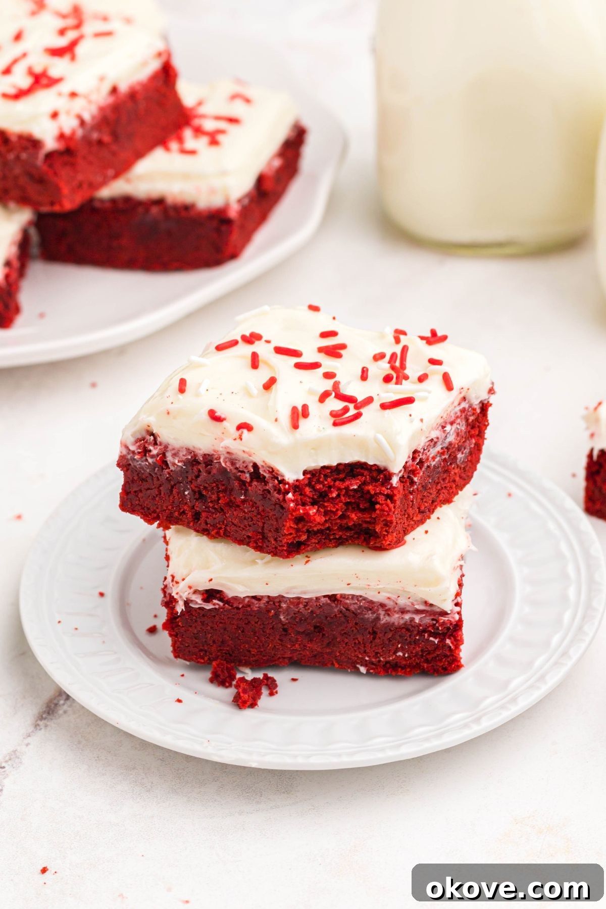 Scarlet Velvet Delights 10 A stack of frosted red velvet bars on a white plate, with one bar showing a bite missing, tempting and delicious.