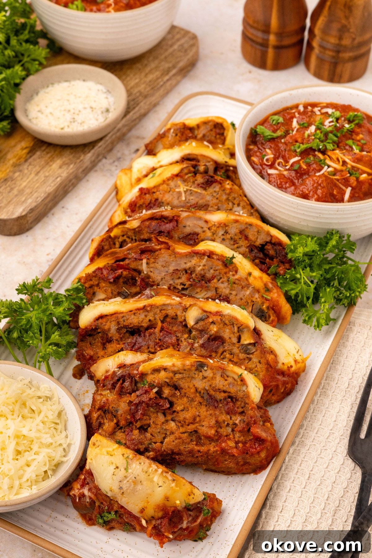 Classic Italian Meatloaf 12 Slices of Italian meatloaf on a rectangle serving dish with extra marinara sauce in a white dish, ready to be enjoyed.