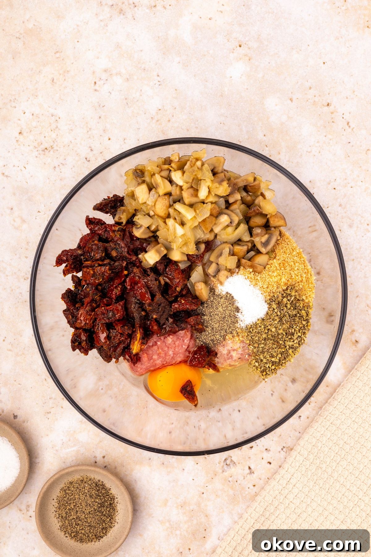Classic Italian Meatloaf 6 Meatloaf ingredients being mixed in a clear glass bowl, showcasing the blend of meats, vegetables, and seasonings.