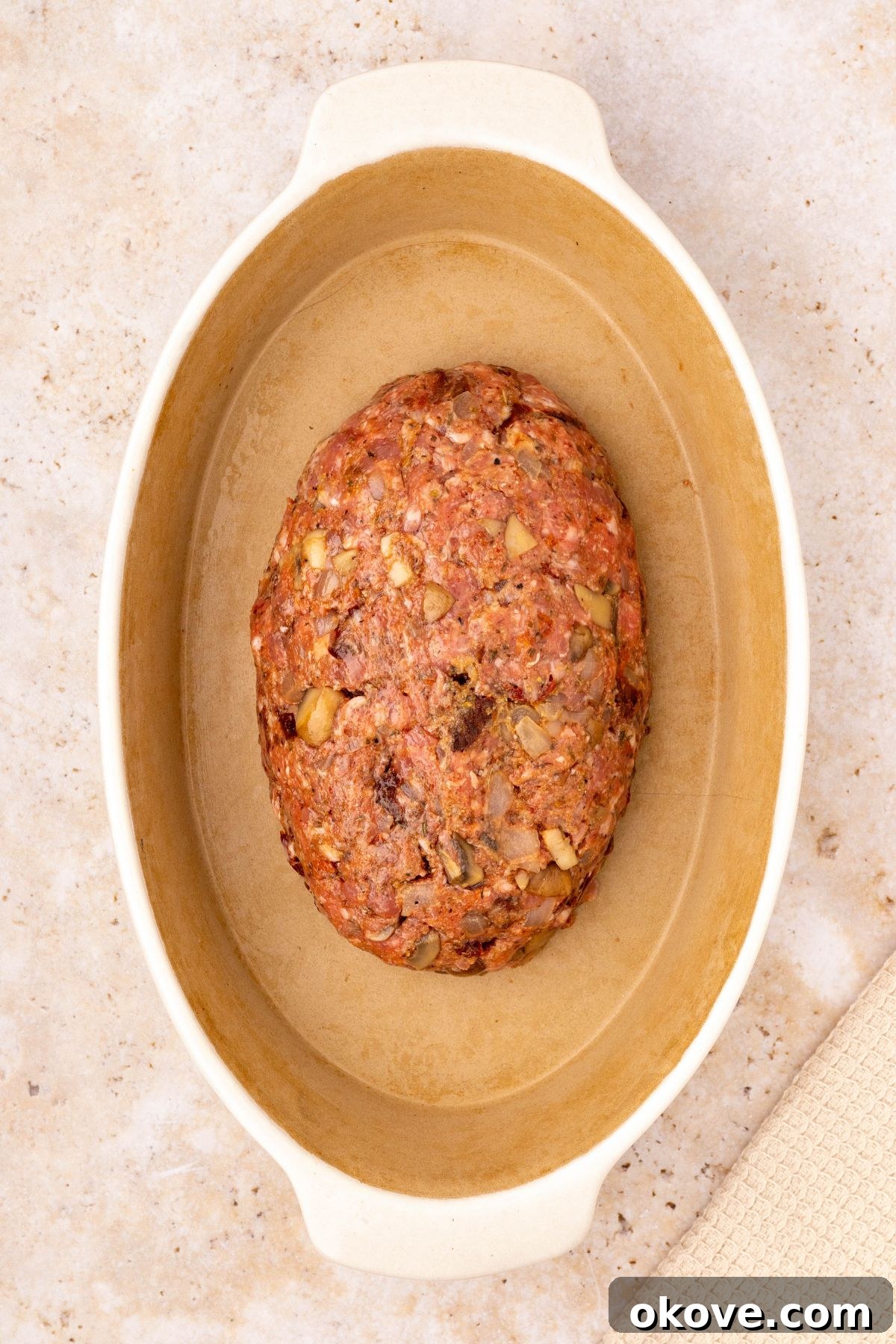 Classic Italian Meatloaf 8 Uncooked meat shaped into a loaf, nestled in an oval casserole dish, with marinara sauce poured generously around it.