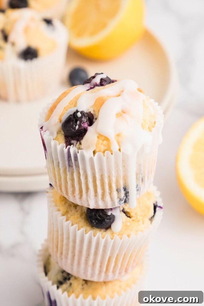 Golden lemon blueberry muffins stacked on a marble board and then drizzled with lemon glaze. These muffins are fluffy and moist, showcasing a perfect bake and vibrant blueberries.