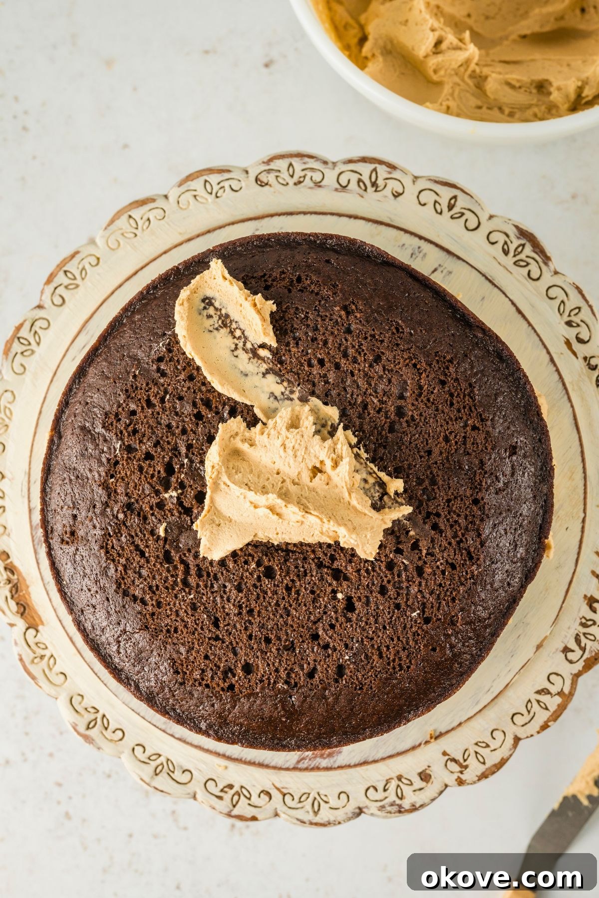 Peanut Butter Chocolate Dream Cake 8 Peanut butter frosting being spread on top of a chocolate cake layer, showing the preparation for stacking.