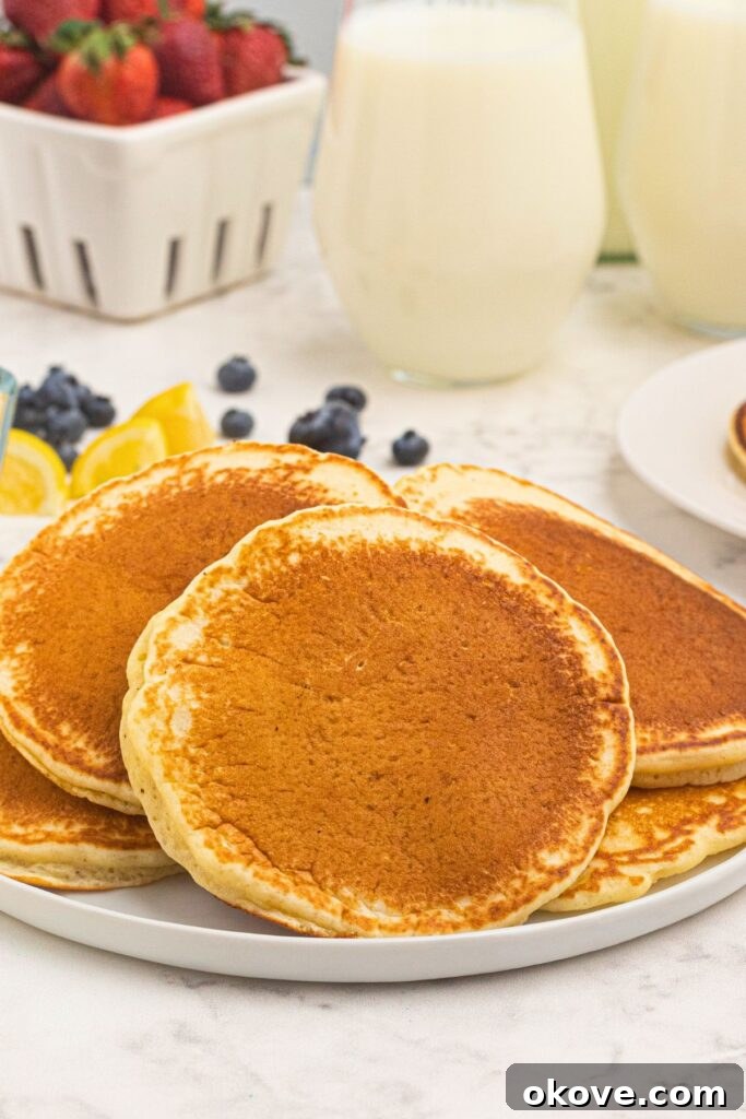 Stacked golden brown and fluffy pancakes on a white plate.