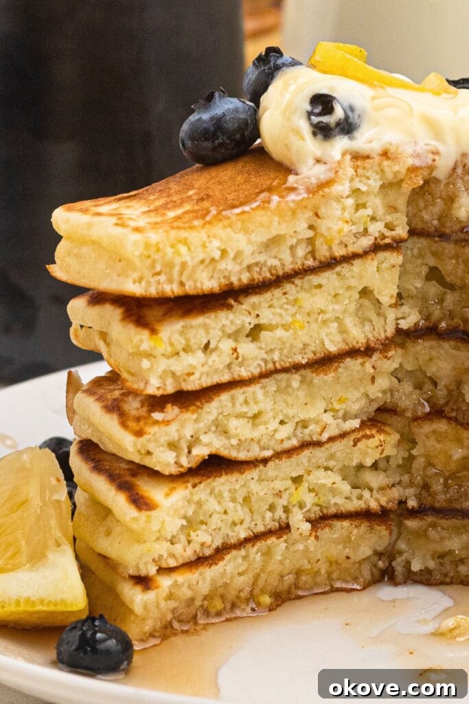 Light and fluffy pancakes stacked on a white plate, drizzled in syrup with butter and blueberries on top.