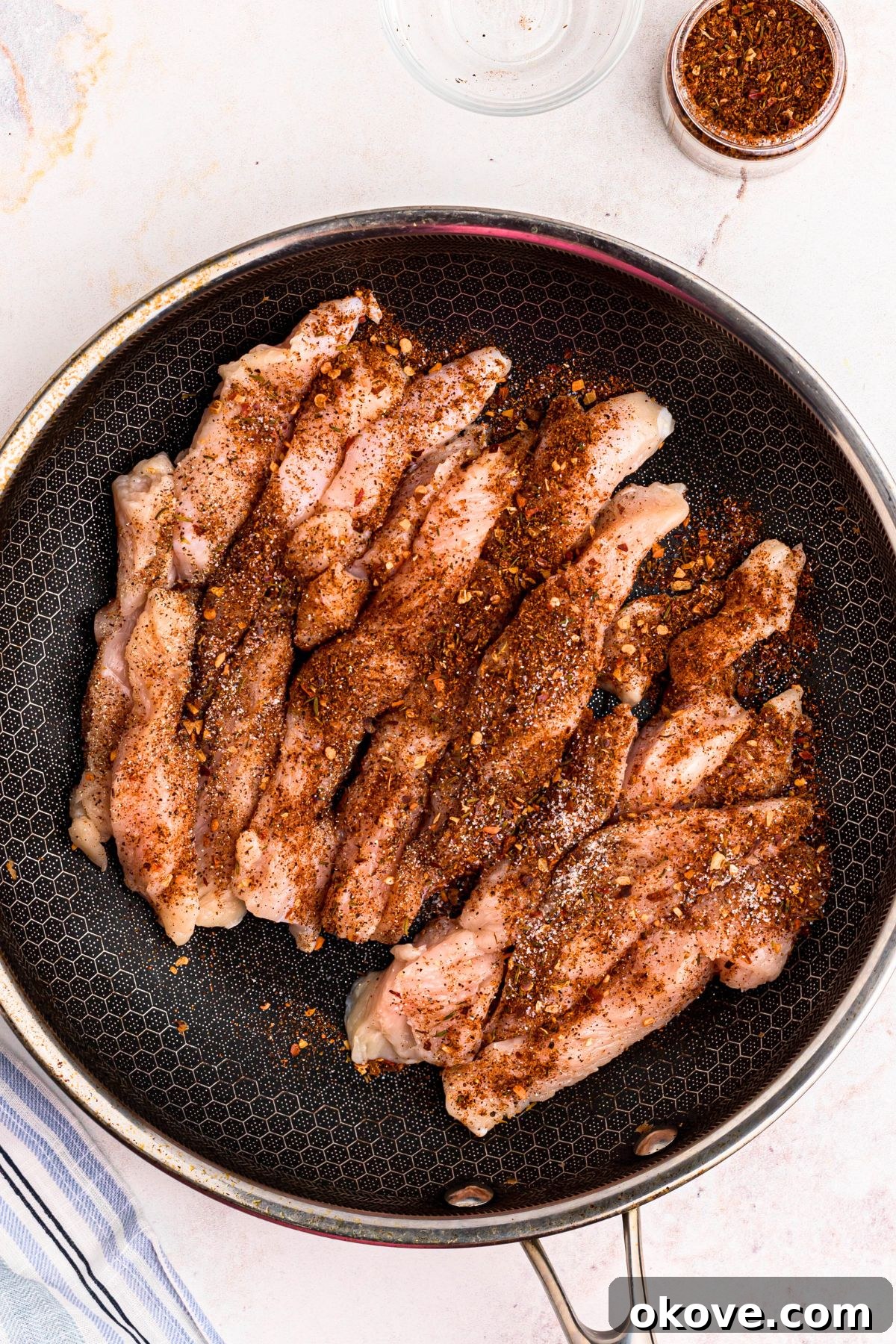 Vibrant Jerk Pasta 4 Chicken strips generously seasoned with jerk spice, salt, and pepper in a large skillet, perfectly prepared for cooking.