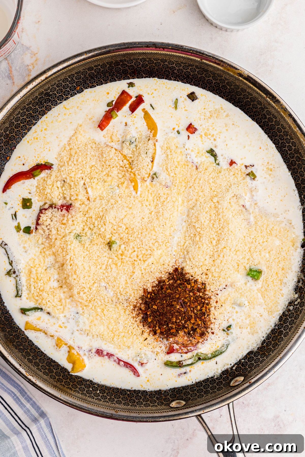 Vibrant Jerk Pasta 6 The creamy Rasta Pasta sauce gently simmering in a large skillet, showing heavy cream, chicken stock, and grated Parmesan cheese blending together to create a luscious consistency.