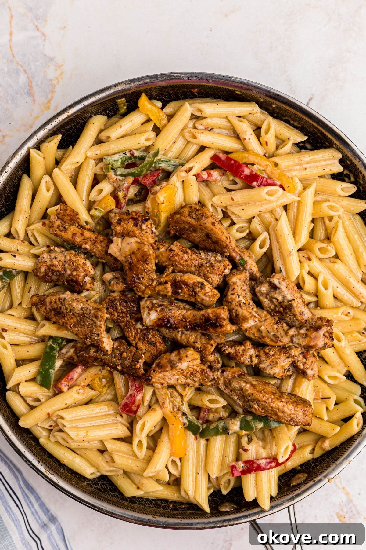 Vibrant Jerk Pasta 7 Finished Rasta Pasta, with cooked penne, rich cheesy cream sauce, sautéed vegetables, and perfectly seasoned chicken, all mixed and ready to serve in a large skillet.