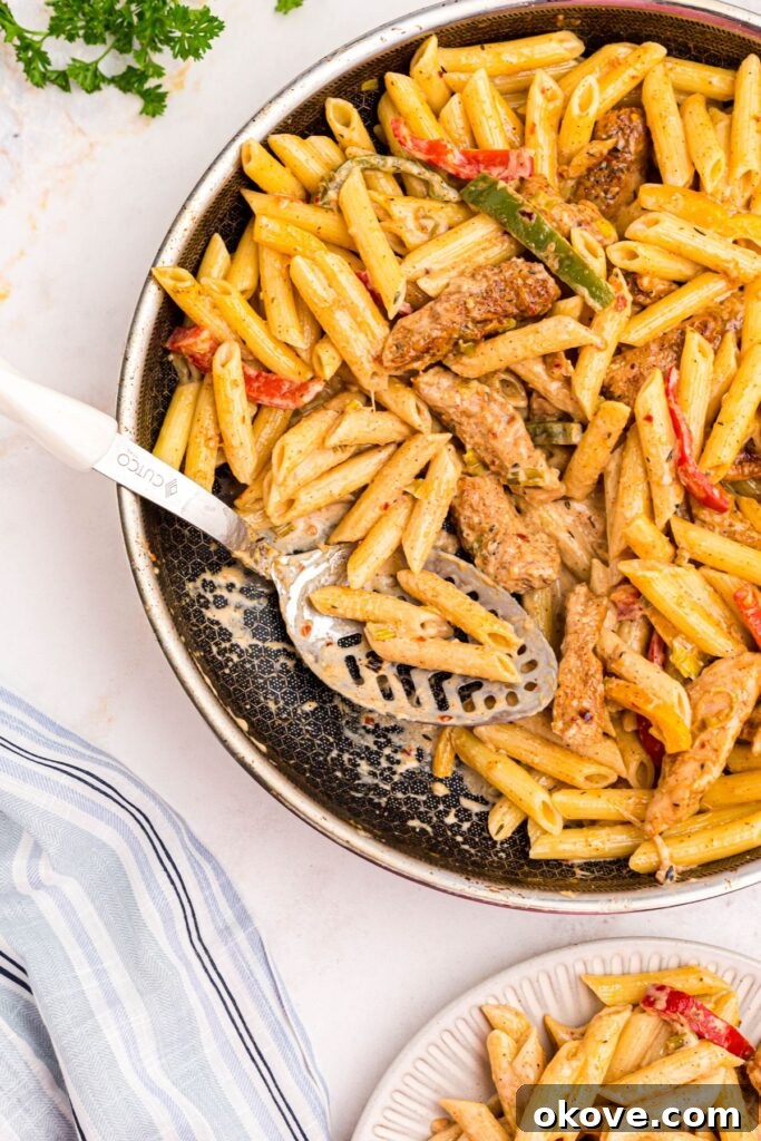 Vibrant Jerk Pasta 8 A large serving spoon nestled in a skillet brimming with rich, creamy Rasta Pasta, complete with tender chicken and colorful vegetables, perfectly ready to be dished out and enjoyed.
