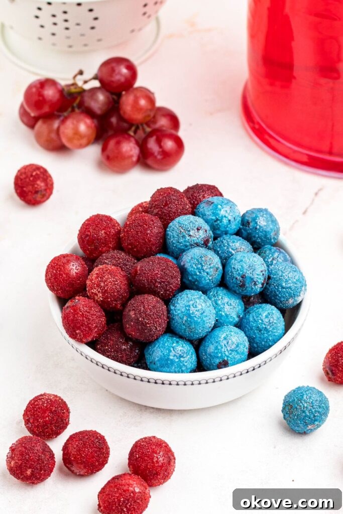 Frosted Grape Jewels 2 Red and blue powdered candy grapes stacked in a white bowl with some scattered on the table. A vibrant, inviting image of the finished candy grapes.