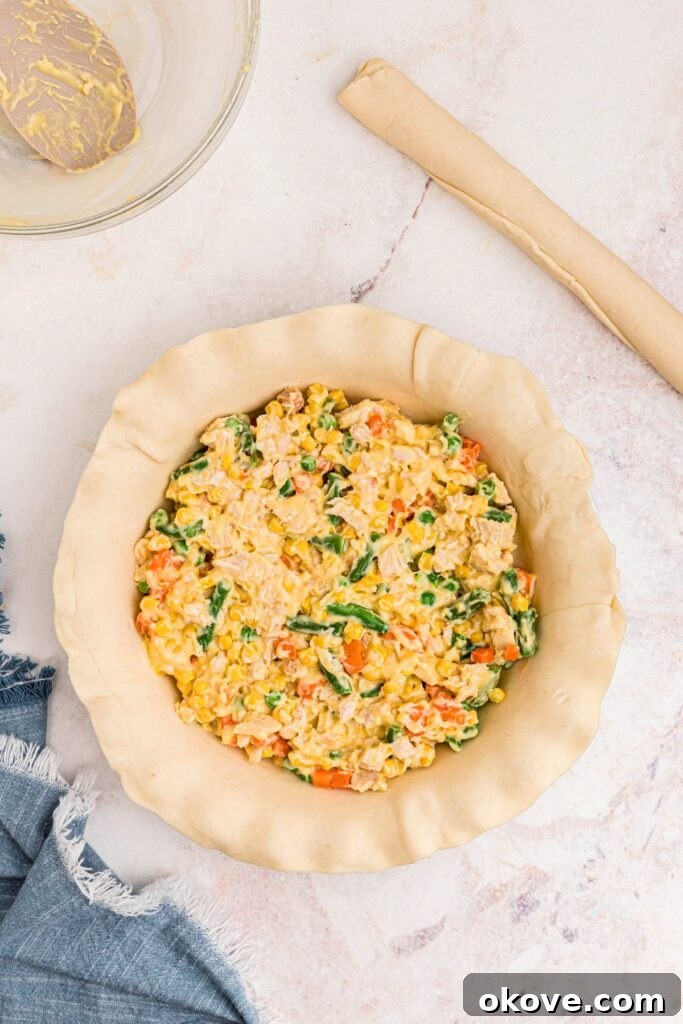 Quick and Cozy Chicken Pot Pie 5 Chicken pot pie filling consisting of chicken, vegetables, and creamy soup, perfectly nestled in a pie pan on a marble table.