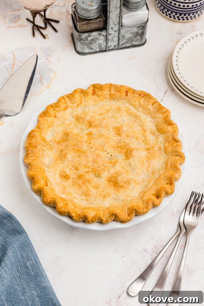 Quick and Cozy Chicken Pot Pie 7 Golden baked chicken pot pie resting on a marble table, flanked by forks and small white plates, ready to be enjoyed.