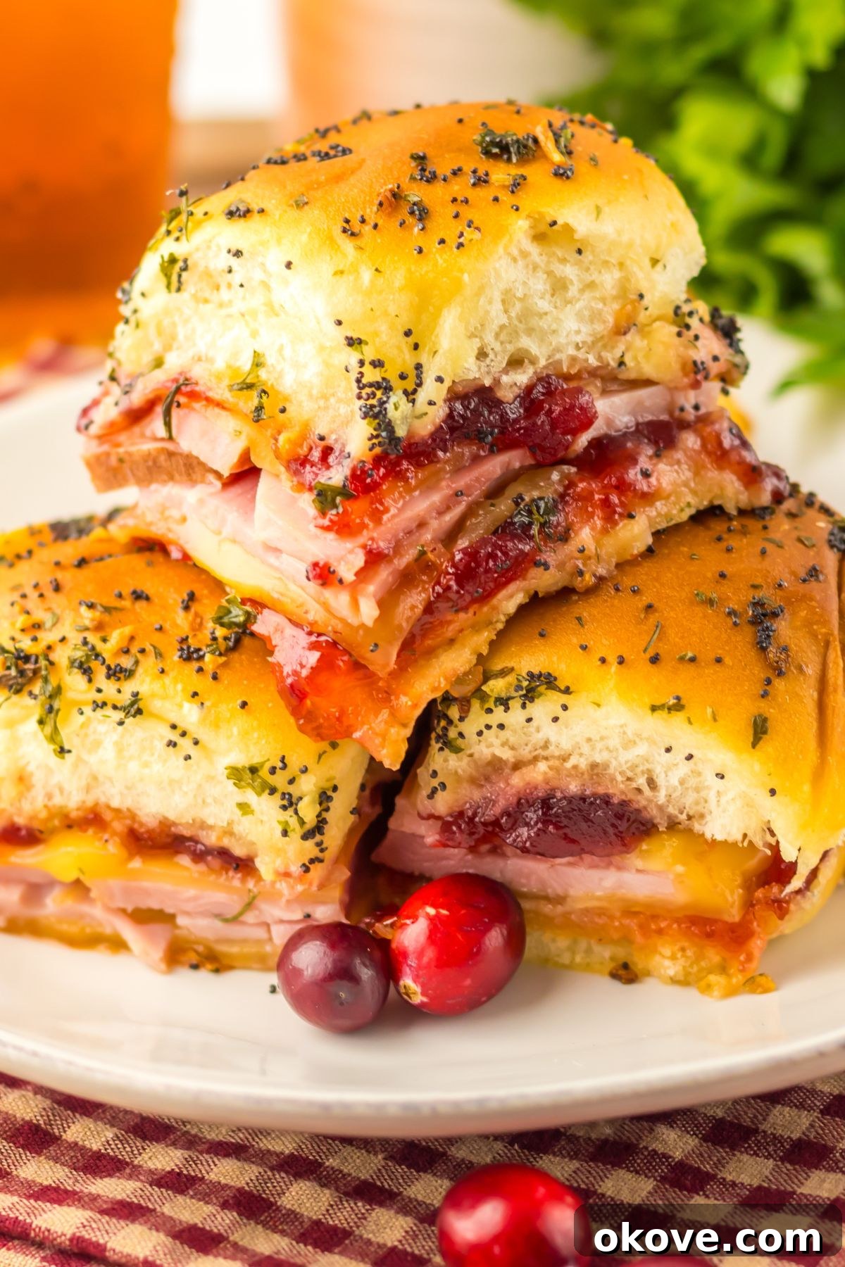 Festive Finger Sandwiches 2 Cranberry and ham sliders stacked on a white plate with red cranberries as a garnish.